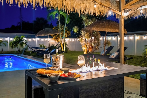 An outdoor bar area with a pool, lounge chairs, and a thatched roof.
