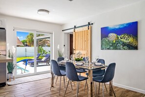 A dining area with a table set for six, a sliding barn door, and a large painting of a sea turtle and fish on the wall.
