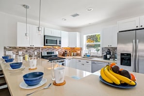 A modern kitchen with white cabinets, stainless steel appliances, and a central island with bowls and a plate of fruit.
