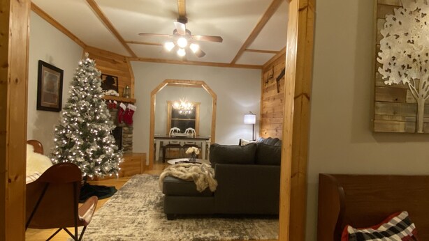 Una sala de estar acogedora con techo de madera, chimenea, árbol de Navidad y una zona de comedor al fondo.