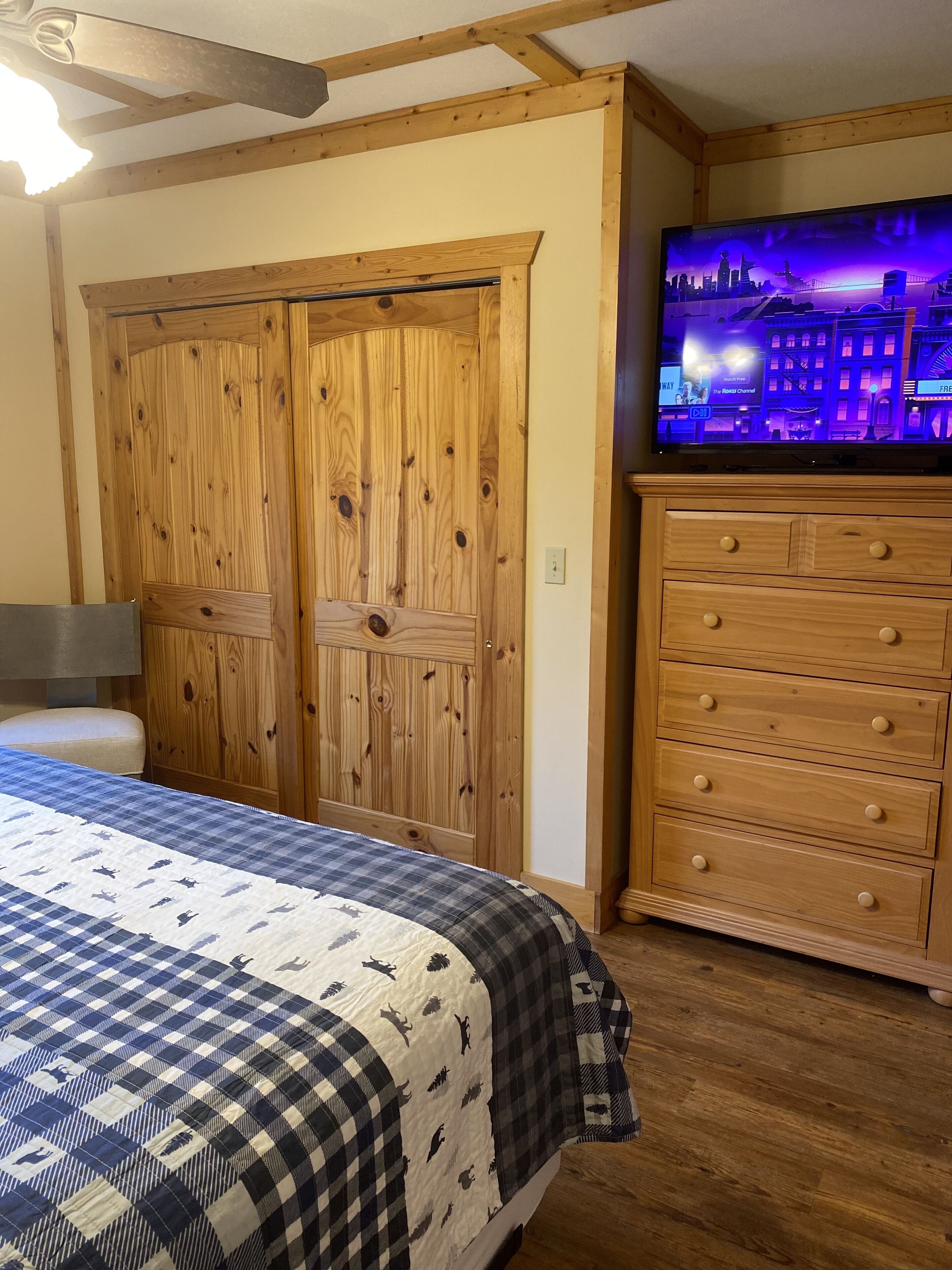 Une chambre avec une armoire en bois, une télévision et un lit recouvert d’une couverture à carreaux.