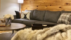 Un salón acogedor con pared de madera, un sofá, una mesita de centro y un plaid de piel.