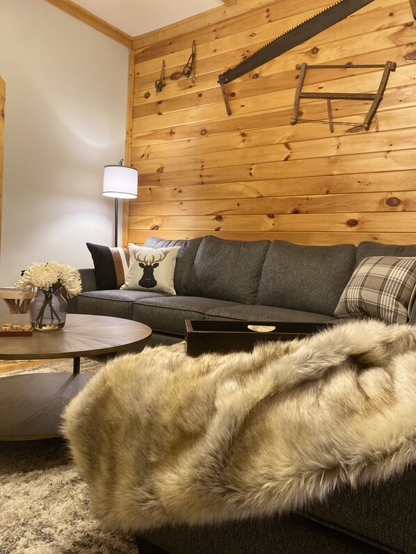 A cozy living room with a wooden wall, a sofa, a coffee table, and a fur throw.
