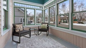 Une véranda avec de grandes fenêtres, deux fauteuils et une petite table.