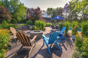 Un patio al aire libre con sillas Adirondack, una fogata y una sombrilla azul.