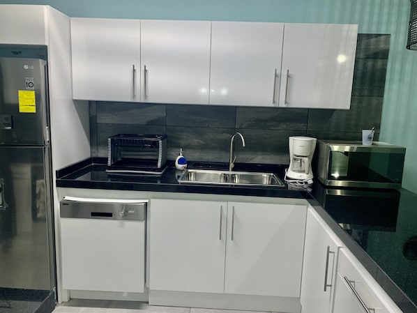 A modern kitchen with white cabinets, a black countertop, a stainless steel sink, a coffee maker, and a microwave. - NEWLY RENOVATED Ocean Front 2 bedroom/ 2 bath, pristine water, divers paradise. (Kralendijk)