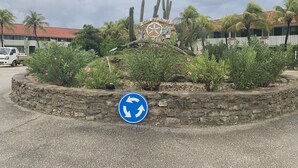 A roundabout with a blue directional sign, a stone wall, and a sign with a palm tree and cactus. - NEWLY RENOVATED Ocean Front 2 bedroom/ 2 bath, pristine water, divers paradise. (Kralendijk)