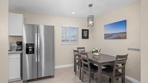 A modern kitchen with a stainless steel refrigerator, a dining table with six chairs, and a wall-mounted picture of a beach scene. - Cozy 2B/1Bth w Great Access to Airport (Fresno)