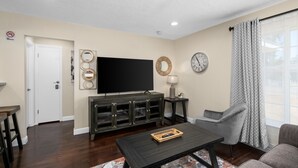 A living room with a flat-screen TV, a dark wood coffee table, a grey armchair, and a patterned rug. - Cozy 2B/1Bth w Great Access to Airport (Fresno)