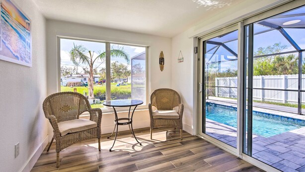 A sunlit room with a pool view, wicker chairs, and a small table. - Englewood Escape w/ Screened-In Pool & Grill! (Englewood)