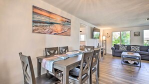 A dining area with a table set for four, a sofa, and a painting of a beach scene. - Englewood Escape w/ Screened-In Pool & Grill! (Englewood)