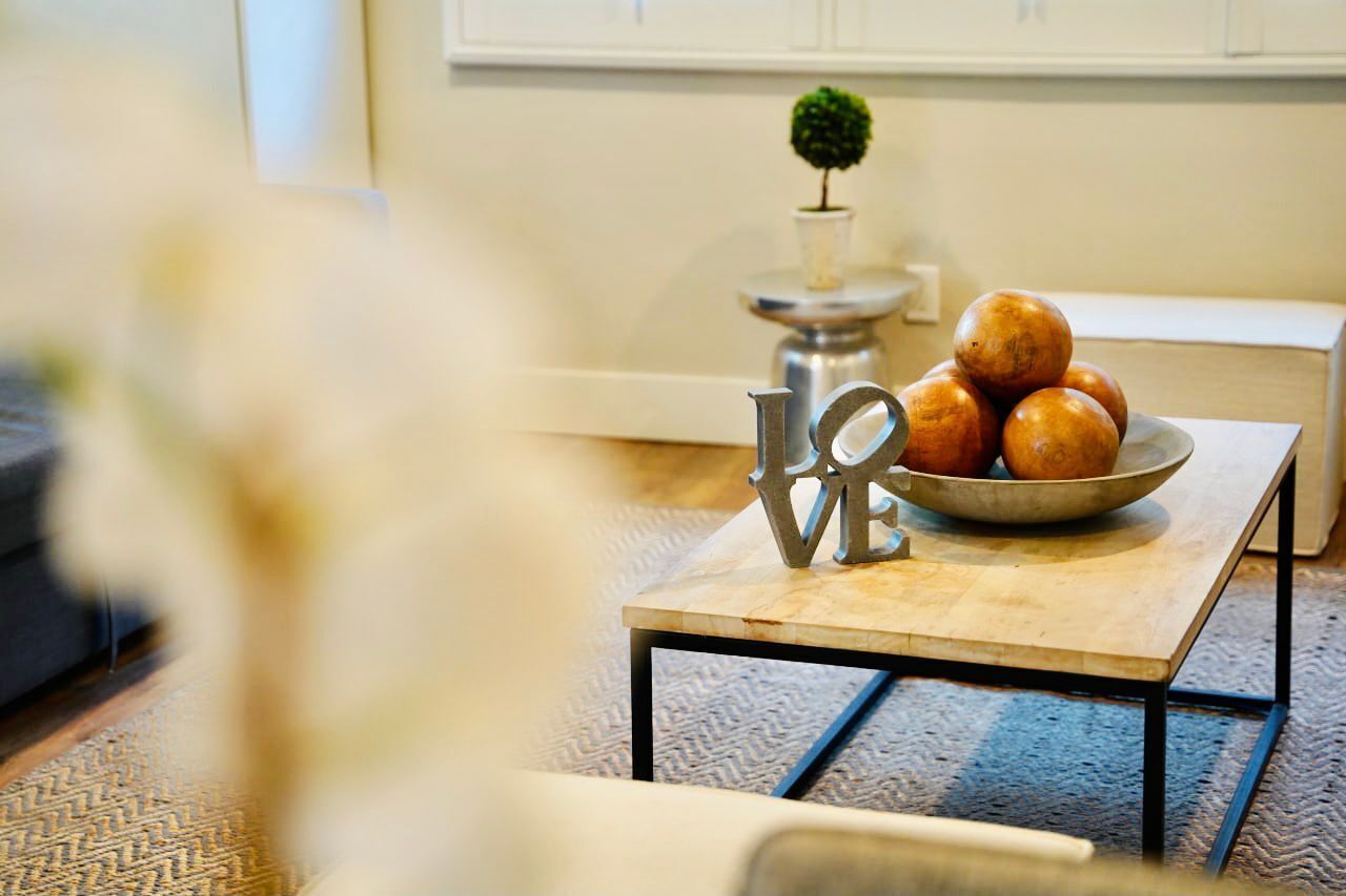 A cozy living room with a small table holding a bowl of fruit and a decorative metal sign.