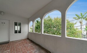 Una habitación con piso de ladrillo, paredes blancas y una ventana con vista a follaje.