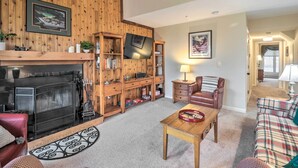 Een gezellige woonkamer met een open haard, houten planken, een televisie en een ruitjesbank.