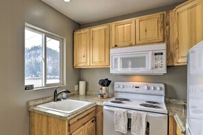 Una cocina con armarios de madera, una estufa blanca, un microondas y una ventana con vistas a un paisaje nevado.