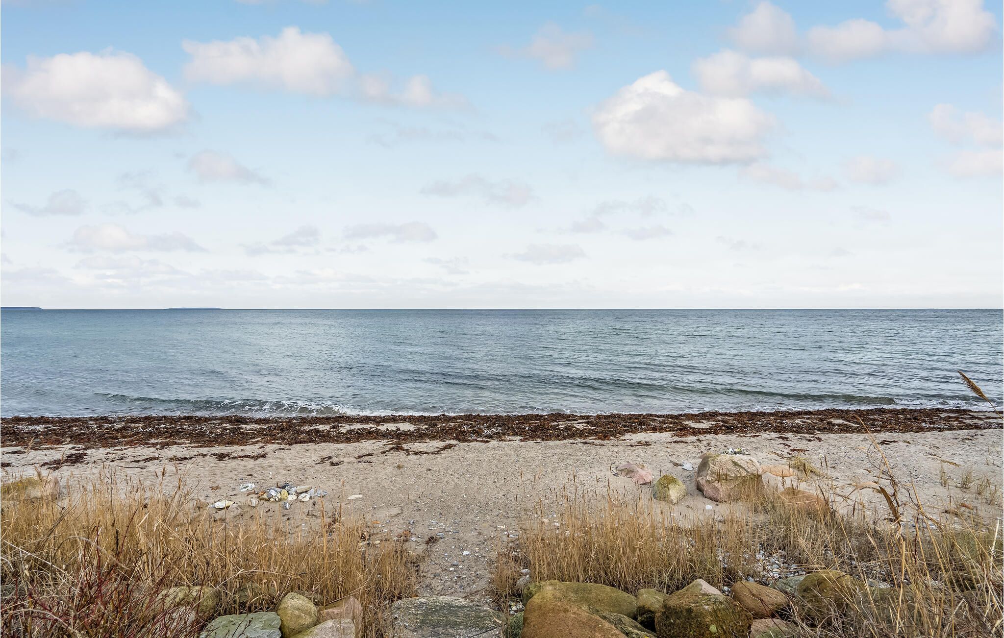Une plage bordée d’une côte rocheuse et baignée par une mer calme, sous un ciel partiellement nuageux.