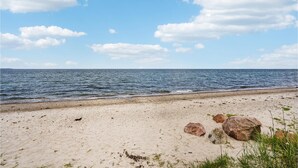 Ein Strand mit sandigem Ufer, großen Felsen und dem Meer unter einem teilweise bewölkten Himmel.