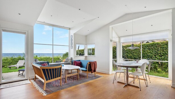 Ein geräumiges Zimmer mit großem Fenster und Meerblick, eine gemütliche Sitzecke mit Sofa und Sesseln sowie ein Esstisch mit Stühlen.