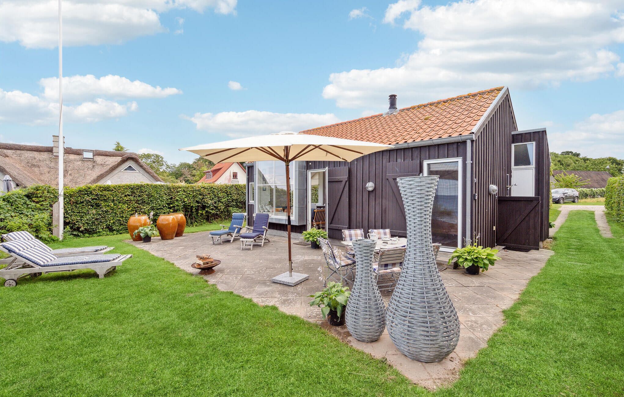 A modern house with a tiled roof, a patio with outdoor furniture, and a large umbrella.