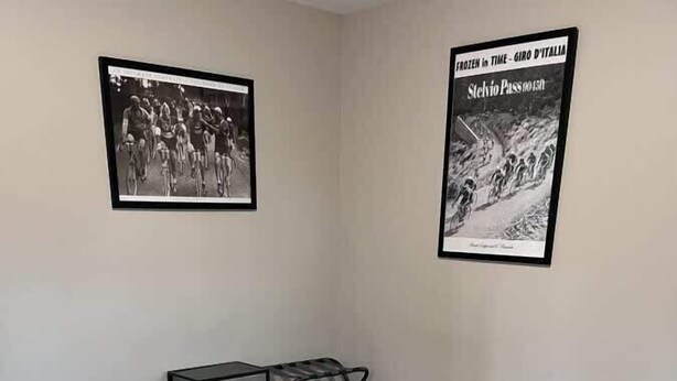 A bedroom with a large bed, a nightstand, a chair, and two framed pictures on the wall.