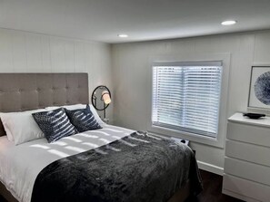 Une chambre à coucher avec un lit, une lampe de chevet, une fenêtre avec des stores et une commode.
