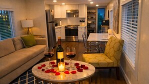 A cozy living area with a sofa, a dining table with rose petals, wine glasses, and a candle.