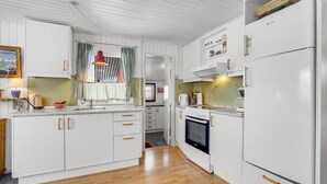 Une cuisine avec des meubles blancs, un plancher en bois et une fenêtre ornée de rideaux à carreaux.