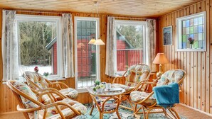 Une pièce chaleureuse aux murs en bois et aux grandes fenêtres, meublée de chaises en osier et d’une petite table ronde.