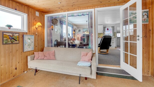 Une pièce chaleureuse avec un canapé, un fauteuil à bascule et un coin repas visible à travers une porte vitrée.