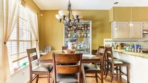 Een eetgedeelte met een houten tafel en stoelen, een kroonluchter en een kast met flessen.