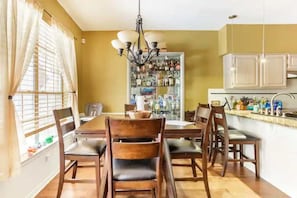 A dining area with a wooden table and chairs, a chandelier, and a cabinet with bottles.