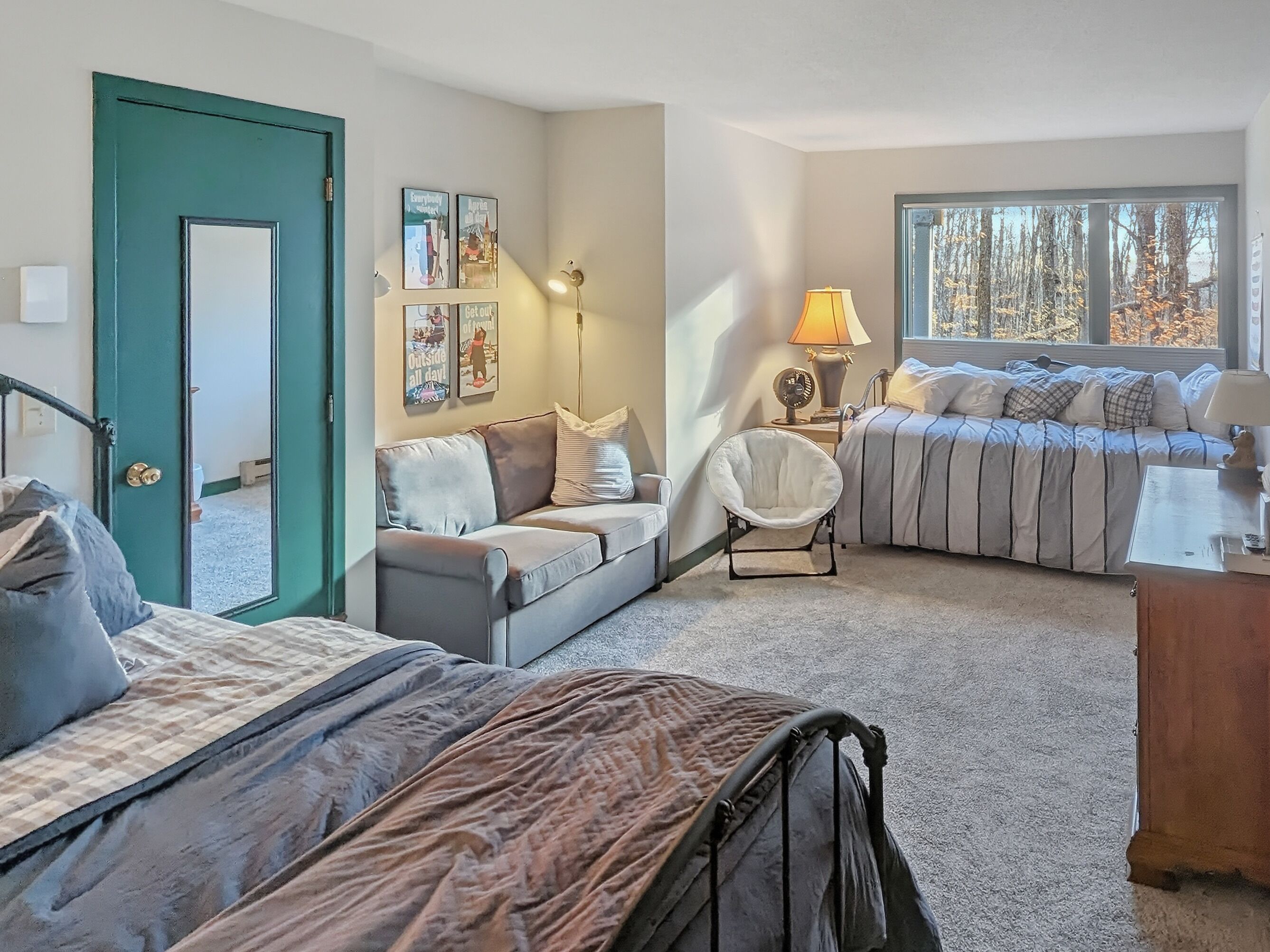 Une chambre confortable avec un lit, un canapé, un fauteuil et une fenêtre donnant sur des arbres.