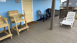 Una terraza de madera con mobiliario exterior, incluyendo sillas y un banco, y una puerta con un letrero.