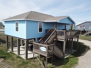 Two-story building with a wooden deck and staircase, set amidst a grassy lawn and gravel path.