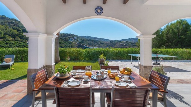 A covered outdoor dining area with a table set for breakfast, overlooking a scenic landscape. - Casa Moreno Cómpeta by Ruralidays (Málaga)