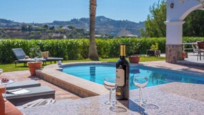 A poolside setting with a bottle of wine and two glasses on a table, overlooking a pool and lush greenery. - Casa Moreno Cómpeta by Ruralidays (Málaga)