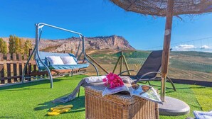Ein Korbstuhl mit Buch und Blumen, ein Schaukelstuhl und Blick auf einen Berg.