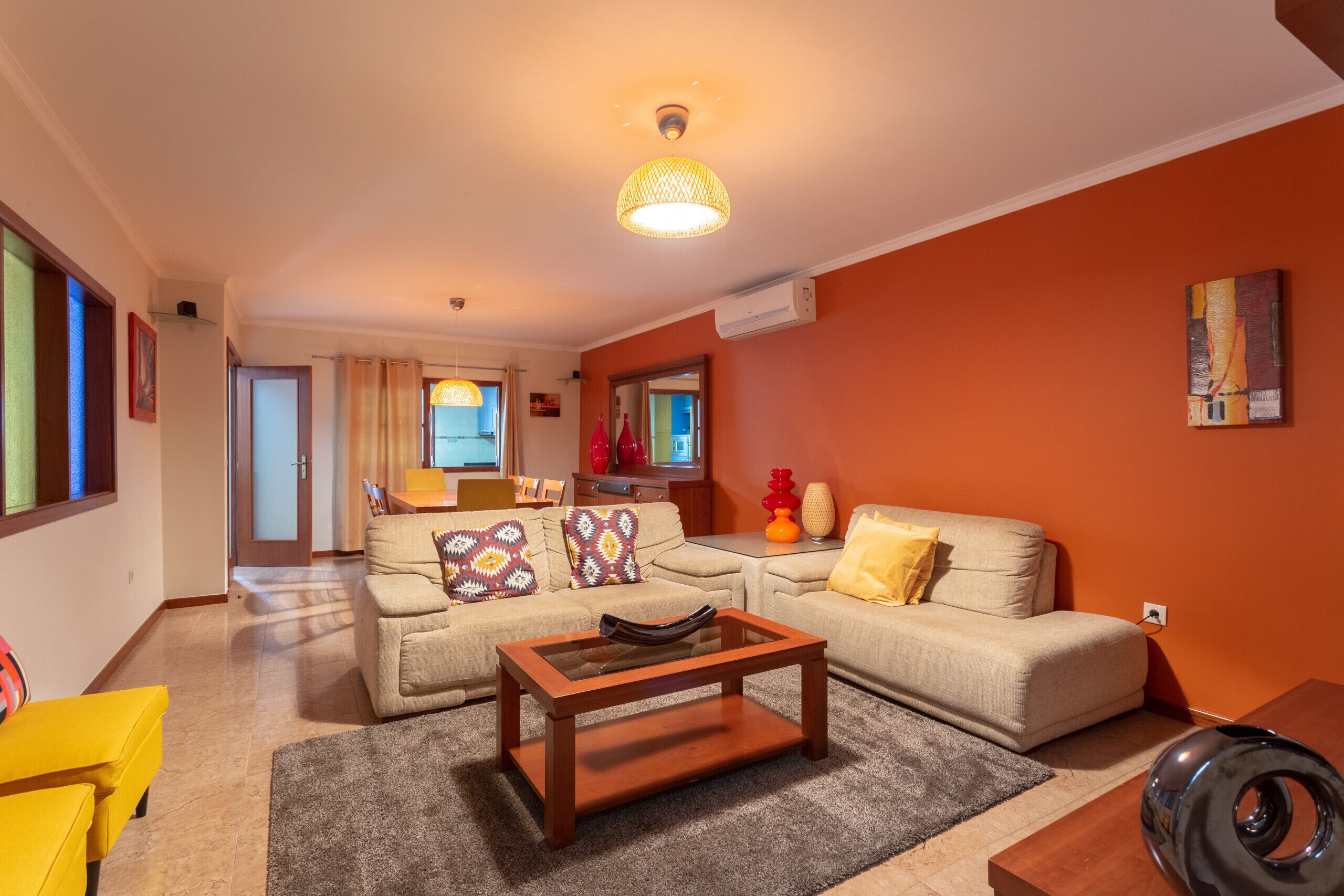 A living room with a sofa, coffee table, and a lamp. There is a window and a door leading to another room.