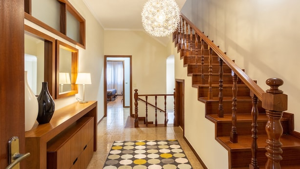A hallway with a wooden staircase, a patterned rug, and a large mirror. - Porto Residence Campanhã (Oporto)