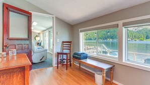 A room with a wooden desk, a chair, a bench, and a large window overlooking a lake.