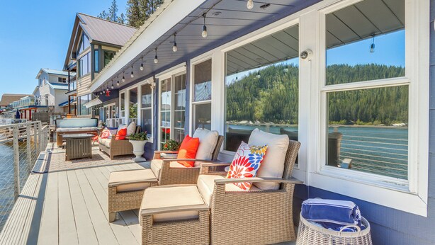 A deck with wicker furniture, a grill, and a view of a lake and forest.