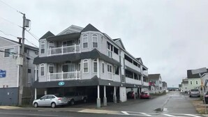 Ein mehrgeschossiges Gebäude mit einem Balkon im zweiten Stock, einer Garage davor und einer Straße im Hintergrund.