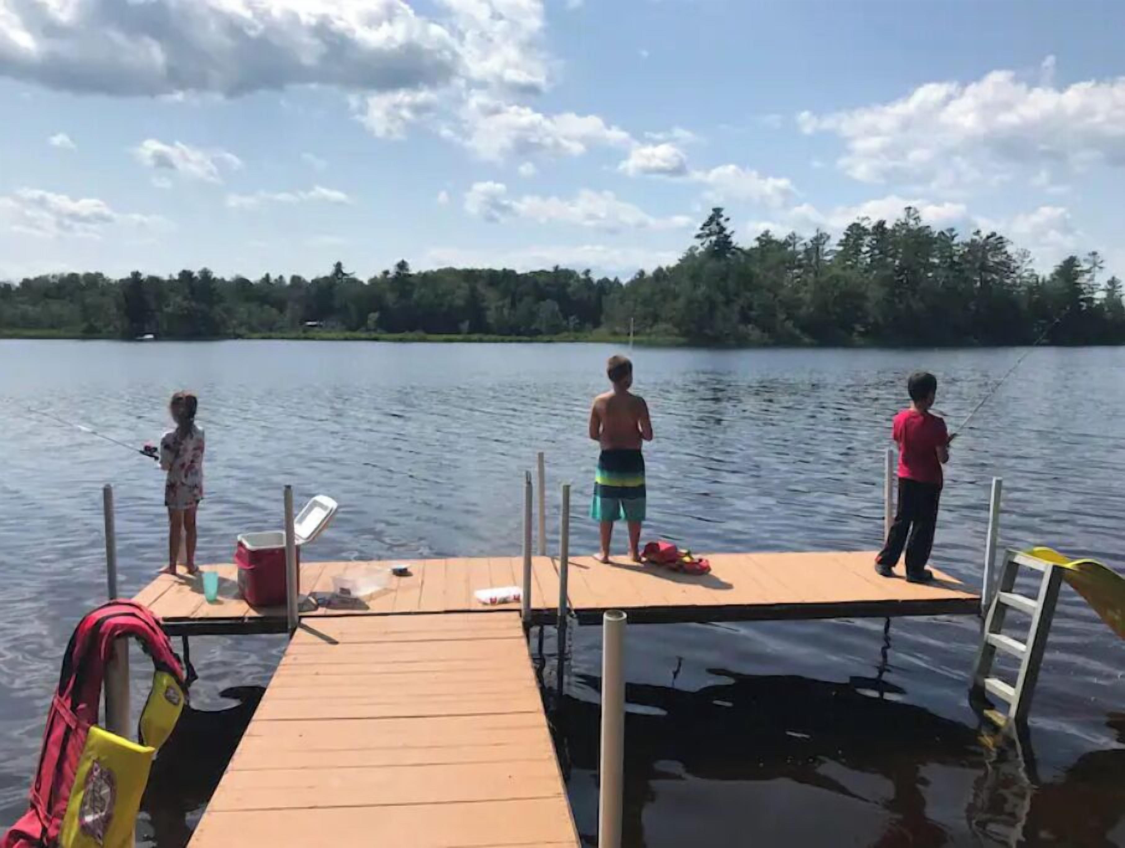 Un moll de fusta que s'endinsa en un llac, amb tres persones pescant.