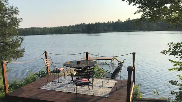 A wooden deck with a table and chairs overlooking a lake. - Tiny Lakeside Cabin-Loons, Bald Eagles & Sunsets (Pittsfield)