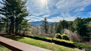 A wooden deck overlooking a landscaped garden with a view of a forest and mountains. - "A Frame Haven" - West Jefferson, NC Mountain Views with Hot Tub (Laurel Springs)