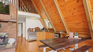 A spacious loft-style kitchen with a wooden ceiling, a brick fireplace, and a dining area with benches.