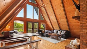 An attic-style room with wooden beams, large windows, a sofa, a coffee table, and a fireplace.