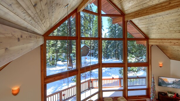Una habitación amplia con ventanas grandes, techo de madera y una zona de estar acogedora con sillas y una mesita.
