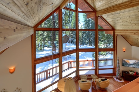 A spacious room with large windows, wooden ceiling, and a cozy seating area with chairs and a small table.