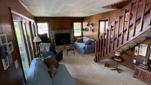 Una sala de estar acogedora con un sofá azul, chimenea, paredes de madera y una escalera.